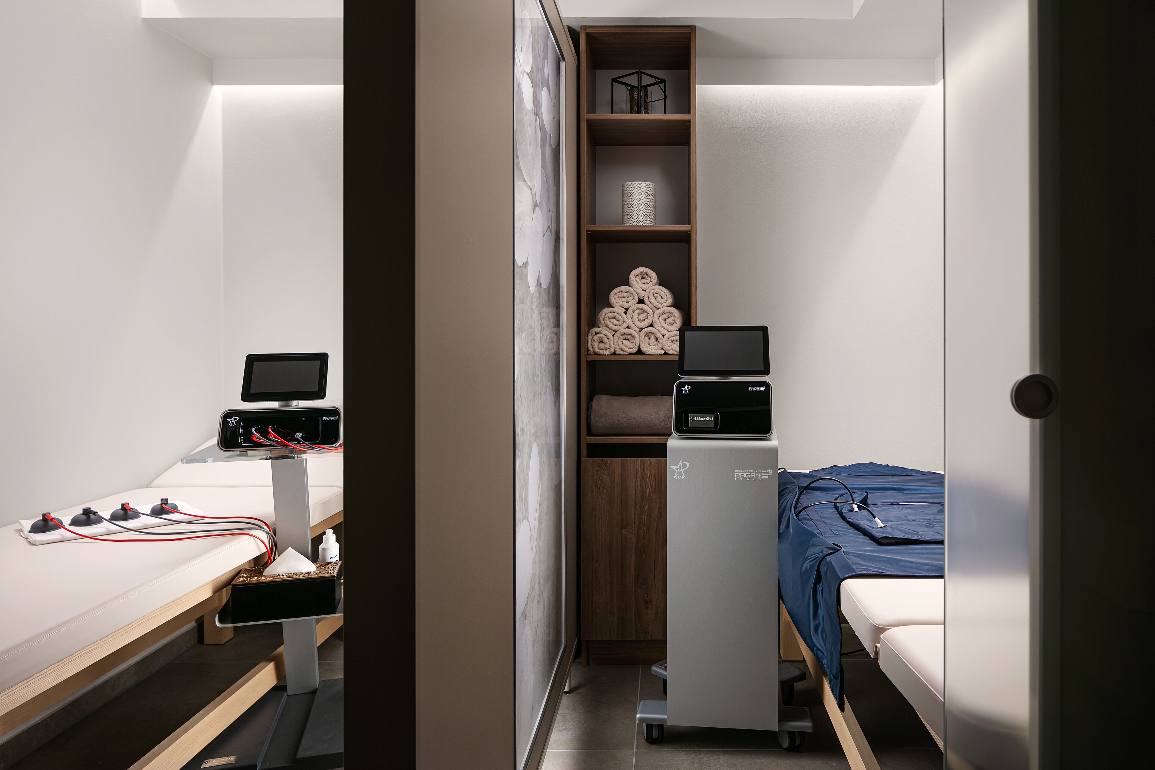 A compact room with a bed, a desk with a computer, a small refrigerator, and a shelf with towels.
