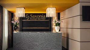 Een receptiebalie met een patroon van marmer, twee kroonluchters, en een bordje met de tekst 'Saxonia Boutique Spa Hotel'.