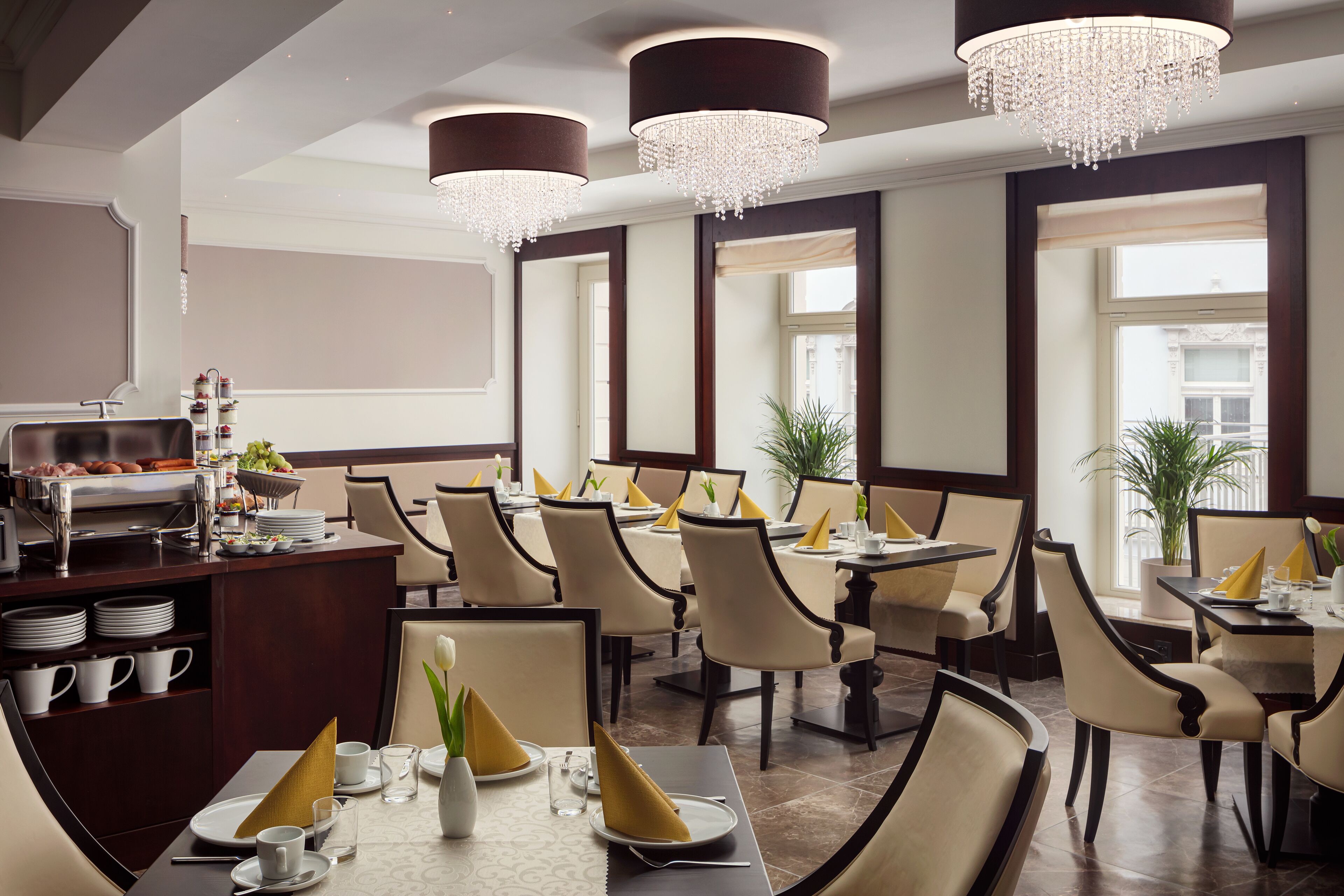A dining area with tables set for service, chandeliers, and a buffet area.