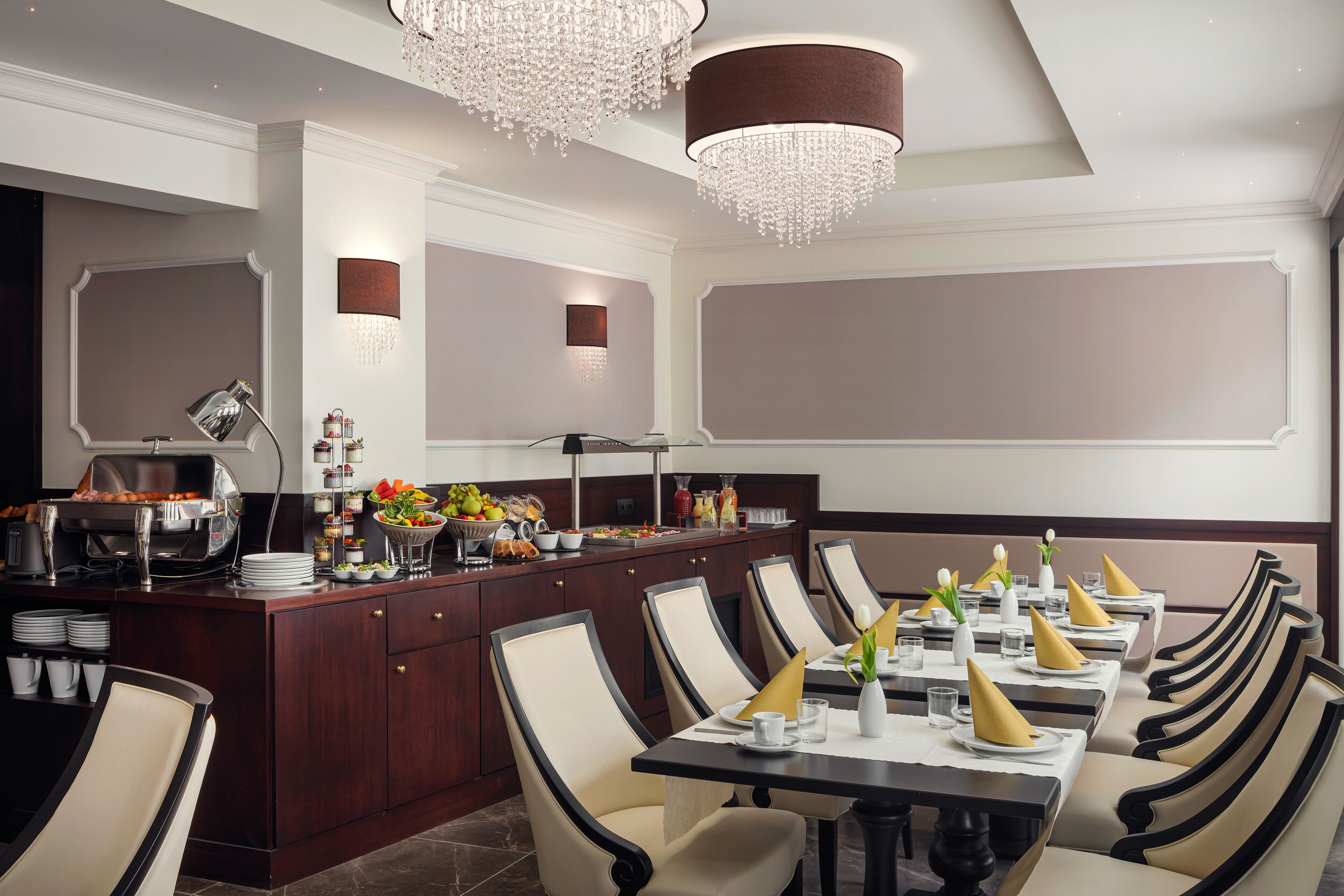 Ein formeller Speisesaal mit einem langen Tisch, der für mehrere Gäste gedeckt ist, einer Buffetstation mit verschiedenen Speisen und stilvollen Kronleuchtern.