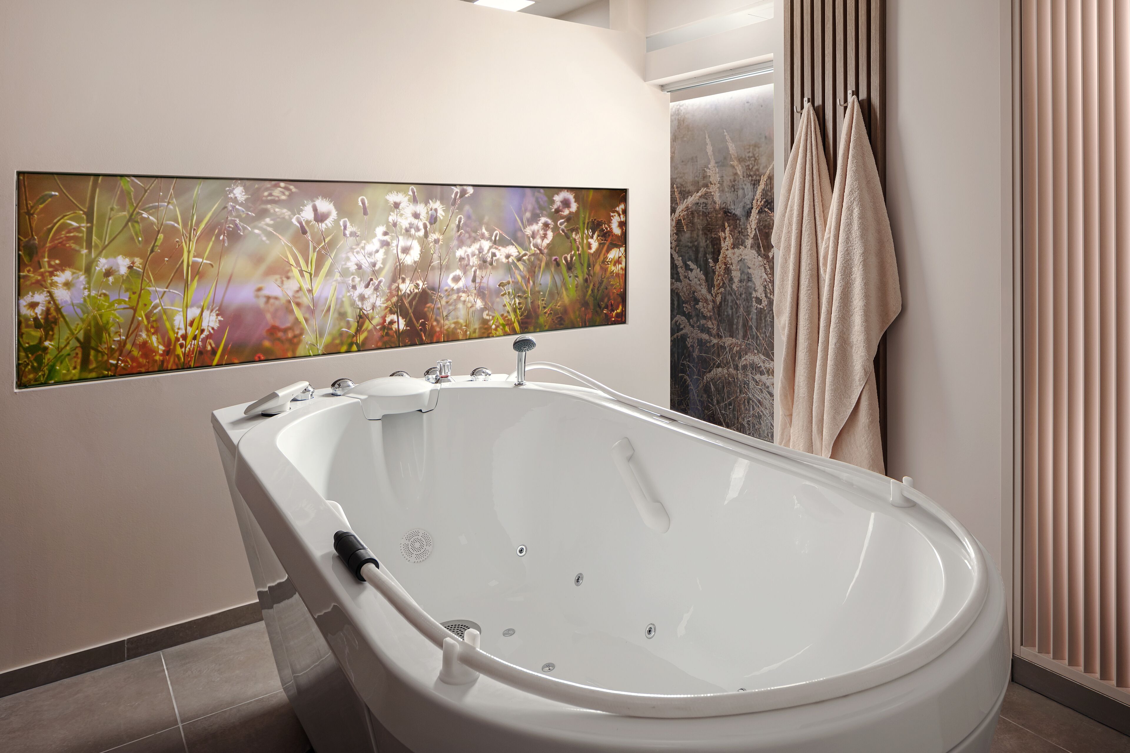 A modern bathroom with a freestanding bathtub, a large wall-mounted TV, and a towel rack.