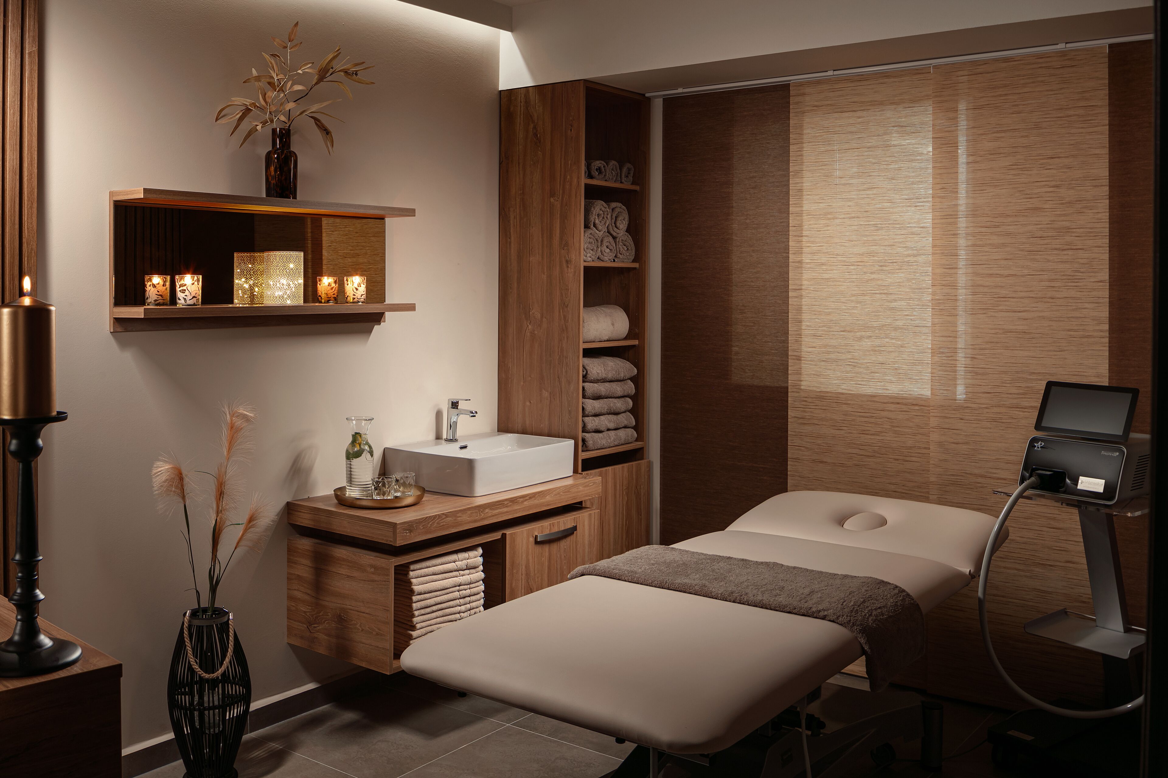 Un spa moderno con una camilla de masaje, un tocador de madera con lavabo, estantes con toallas y un equipo de masaje.