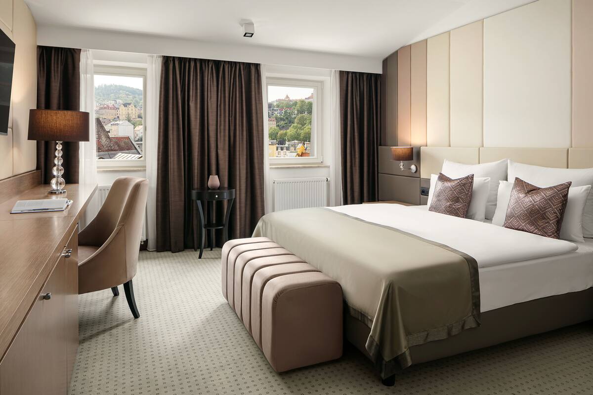 Habitación de hotel con una cama grande, un escritorio, una silla y vistas de la ciudad a través de la ventana.