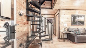 A wooden interior with a kitchen area, a spiral staircase, a sofa, and a painting on the wall.