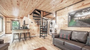 A wooden cabin interior with a living area, kitchen, and a spiral staircase.