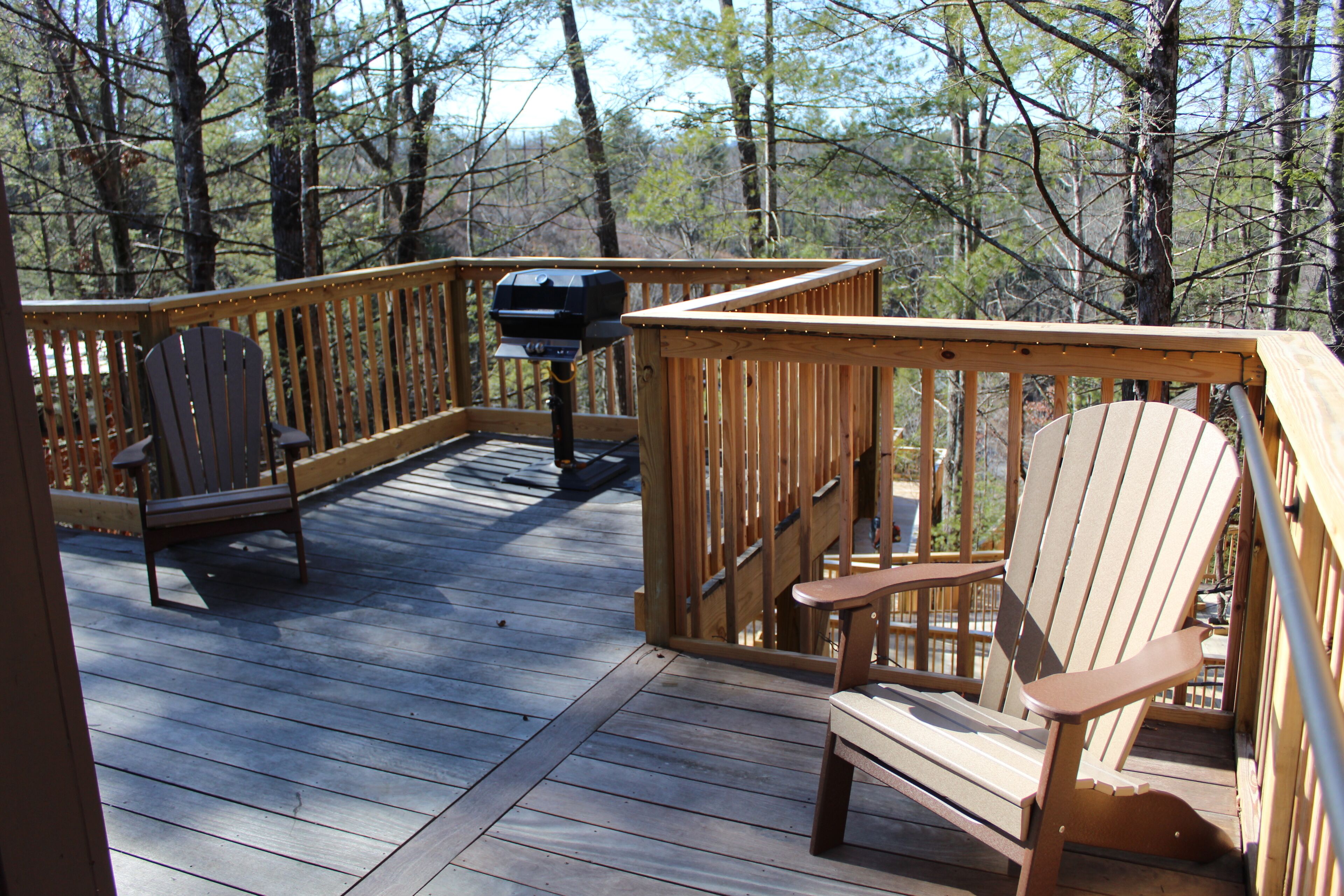 Una terraza de madera con dos sillas Adirondack y una parrilla.