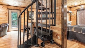 L’intérieur d’un chalet en bois comprend un escalier en colimaçon, un lit, une chaise et un coin repas.