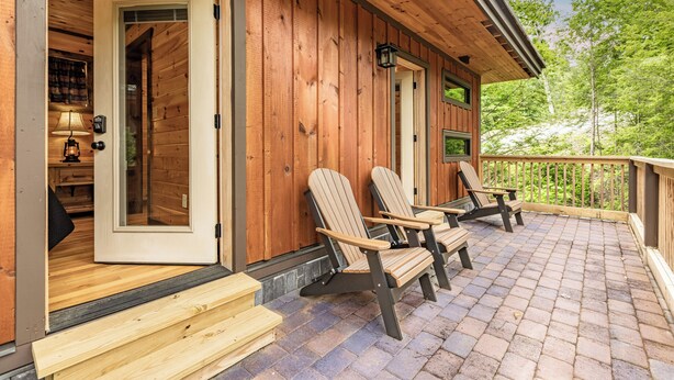 Une cabane en bois dotée d’un porche, de deux fauteuils Adirondack et d’une terrasse en bois.