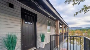A house with a dark front door, white siding, and a balcony with a railing overlooking a body of water. - Lakefront Elegance | Boat Launch | Hot Tub | Dock (Hot Springs)