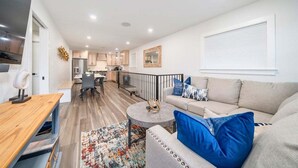 A modern living room with a sofa, coffee table, and a dining area in the background. - Lakefront Elegance | Boat Launch | Hot Tub | Dock (Hot Springs)