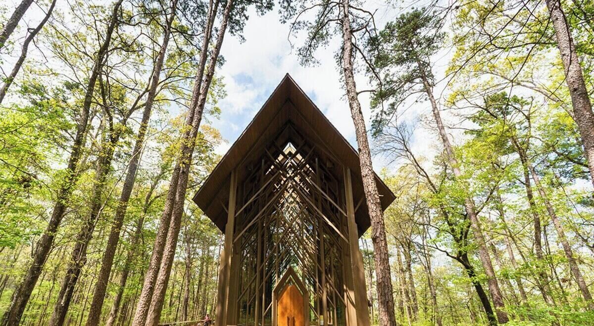 A wooden cabin structure in a forest with a triangular roof and a central opening.