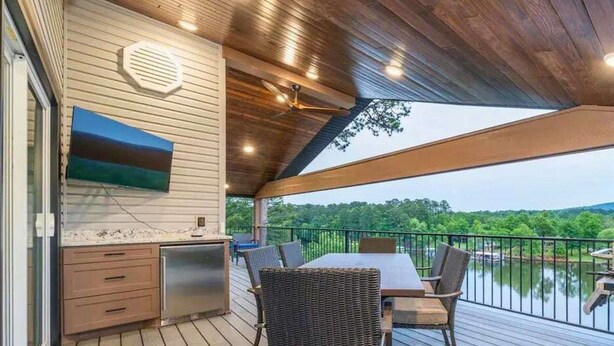 A covered outdoor area with a dining table and chairs, a built-in grill, and a view of a lake. - Lakefront Elegance | Boat Launch | Hot Tub | Dock (Hot Springs)
