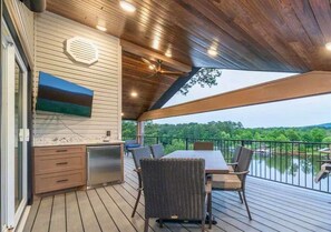 A covered outdoor area with a dining table and chairs, a built-in grill, and a view of a lake.