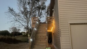A wooden staircase leading to a house with a garage, surrounded by trees and a sandy ground. - Luxury Golf Villa w/ Hot Tub  Stunning Golf Course Views Near OBX Beaches (Kitty Hawk)