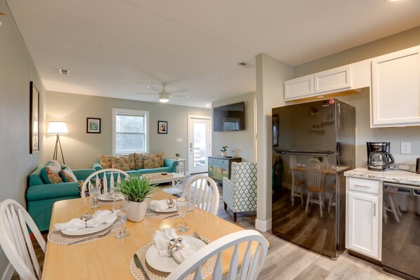 A modern kitchen with a stainless steel refrigerator, white cabinets, and a dining area with a table set for four. - Luxury Golf Villa w/ Hot Tub Stunning Golf Course Views Near OBX Beaches (Kitty Hawk)