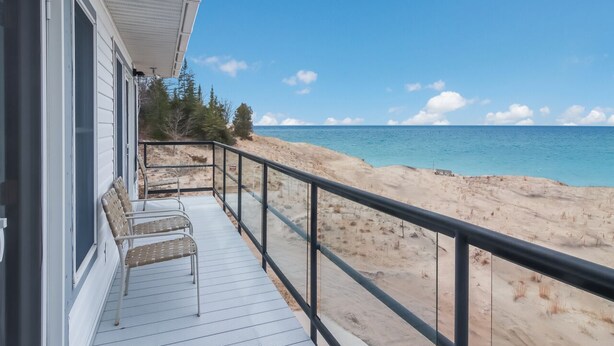 A beach house with a wooden deck and a railing overlooking a sandy beach and ocean. - Griners Life Saving$ Station on Lake Michigan w/ Private Beach, Pet-Friendly (Frankfort)