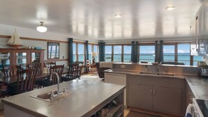 A kitchen with a large island, dining area with chairs, and a view of the ocean. - Griners Life Saving$ Station on Lake Michigan w/ Private Beach, Pet-Friendly (Frankfort)