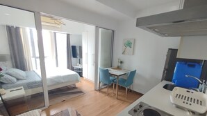 Une chambre d’hôtel comprenant un lit, un bureau, une chaise, un coin cuisine et une porte coulissante donnant sur une autre pièce.