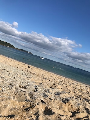 A beach with pebbly sand, a clear blue sky, and a distant view of a boat on the water. - Lovely cottage, creekside village, spacious garden, lots of parking (Falmouth)
