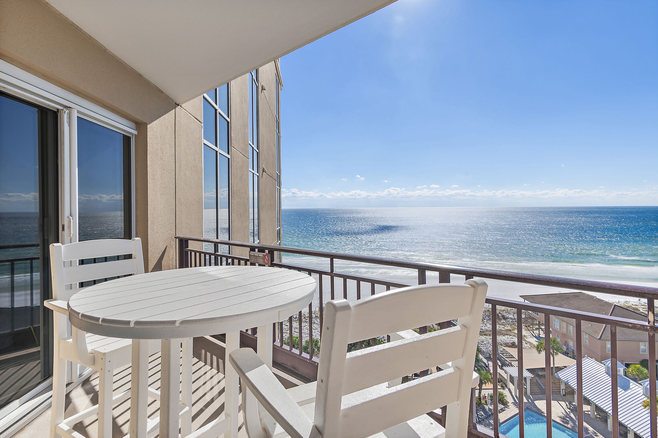 A balcony with a white table and chairs, overlooking a beach and ocean.