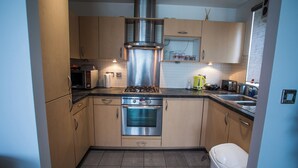 A compact kitchen with stainless steel appliances, wooden cabinets, and a tiled backsplash. - Remarkable 2-bed Apartment With Sea View (London)