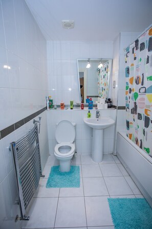 A bathroom with a toilet, sink, and mirror. There are toiletries on the sink counter and a towel rack. - Remarkable 2-bed Apartment With Sea View (London)