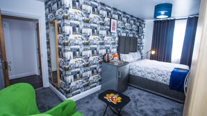 A hotel room with a patterned wallpaper, a bed with a floral duvet, a desk with a lamp, and a green armchair. - Remarkable 2-bed Apartment With Sea View (London)