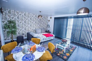 A modern living room with a sofa, dining table, and chairs. There is a small table with decorative items and a plant. - Remarkable 2-bed Apartment With Sea View (London)