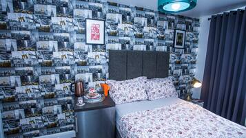 A hotel room with a patterned wallpaper, a bed with floral bedding, a nightstand with a lamp, and a coffee maker.