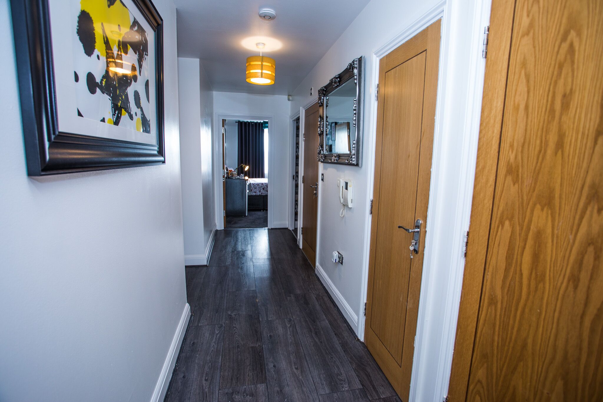 A hallway with dark wooden flooring, white walls, and a framed artwork on the left.
