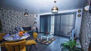 A modern living room with a dining area, featuring a sofa, a coffee table, and a dining table set with blue and white plates. - Remarkable 2-bed Apartment With Sea View (London)