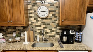 A kitchen with wooden cabinets, a granite countertop, a Bosch dishwasher, a coffee maker, and a clock on the wall. - Beautifully Decorated Condo with Pool and Fitness Center! Pet Friendly! (Saint Simons Island)