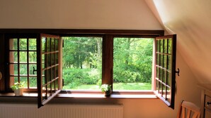 Una habitación con un ventanal grande, vigas de madera en el techo, un radiador y una silla.