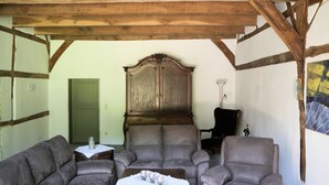 Una habitación con techo de madera, un mueble de madera grande, dos sofás grises, una mesita de madera y una silla.