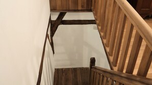 Una escalera de madera con barandilla que conduce a un rellano con un muro y un armario de madera.