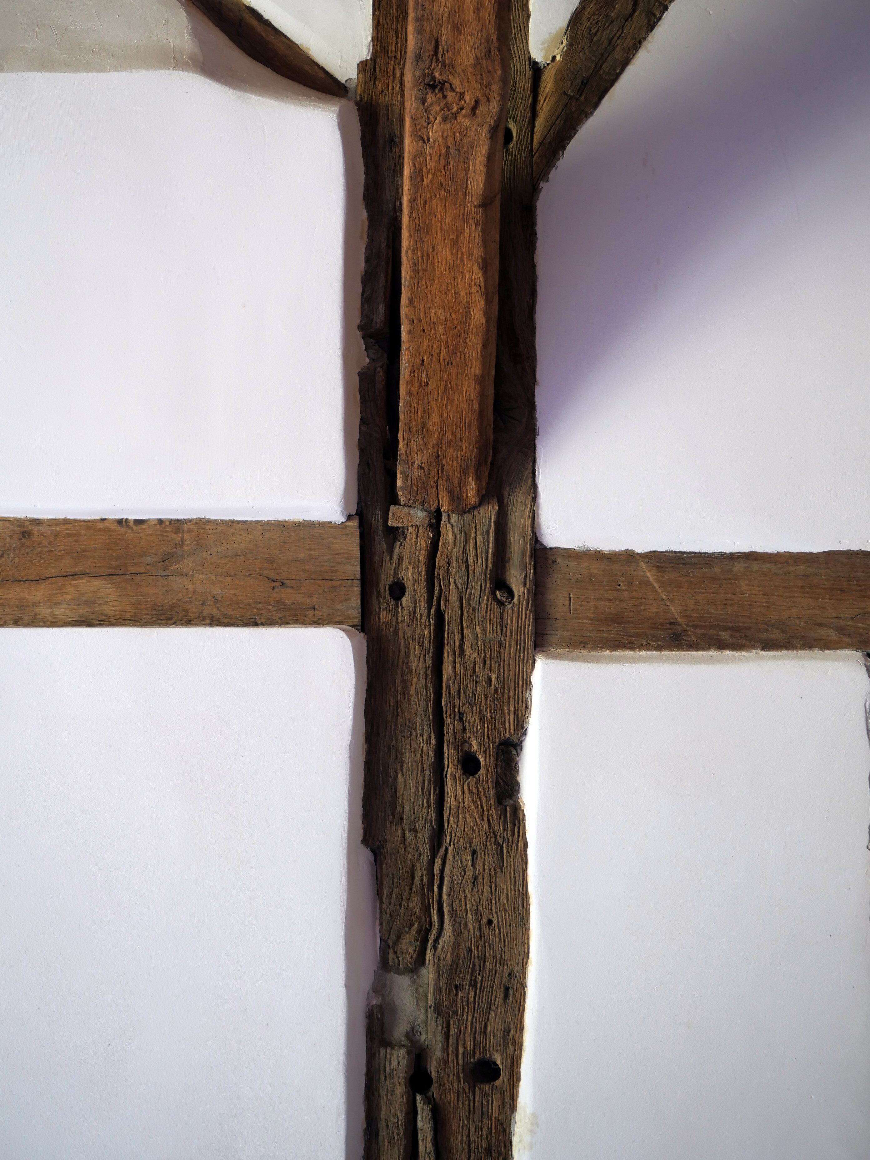 Eine Holzträgerkonstruktion mit deutlichen Gebrauchsspuren und Löchern, vermutlich ein Teil der Bausubstanz.