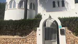 A white building with arched windows and a stone wall in front. - Villa with sea view and pool in Cala D' Or (Santanyí)