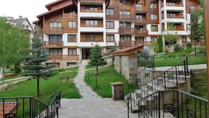 A multi-story building with balconies, a stone pathway leading to the entrance, and a small tree in the foreground. - Luxury Apartments St Ivan Rilski SPA 4 (Bansko)