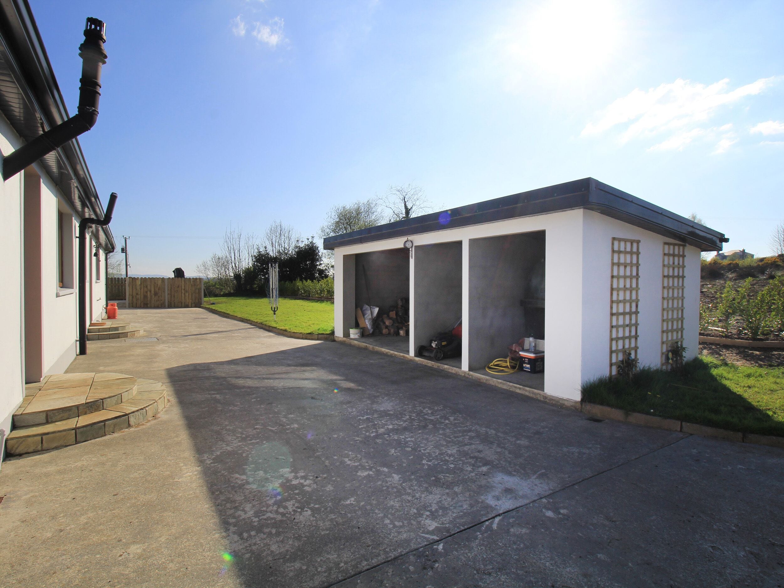 A garage with a covered area, a concrete driveway, and a lawn.