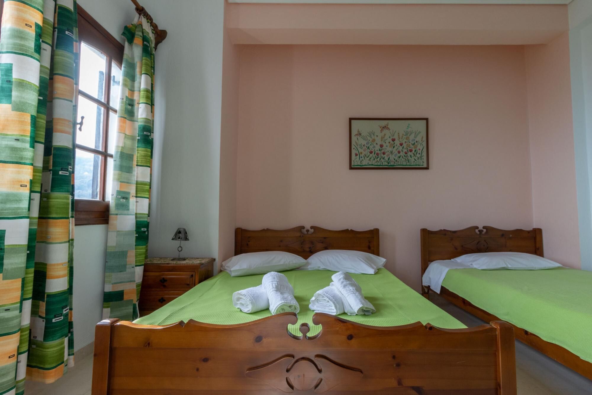A bedroom with two wooden beds, green bedspreads, white pillows, and a small bedside table with a lamp.