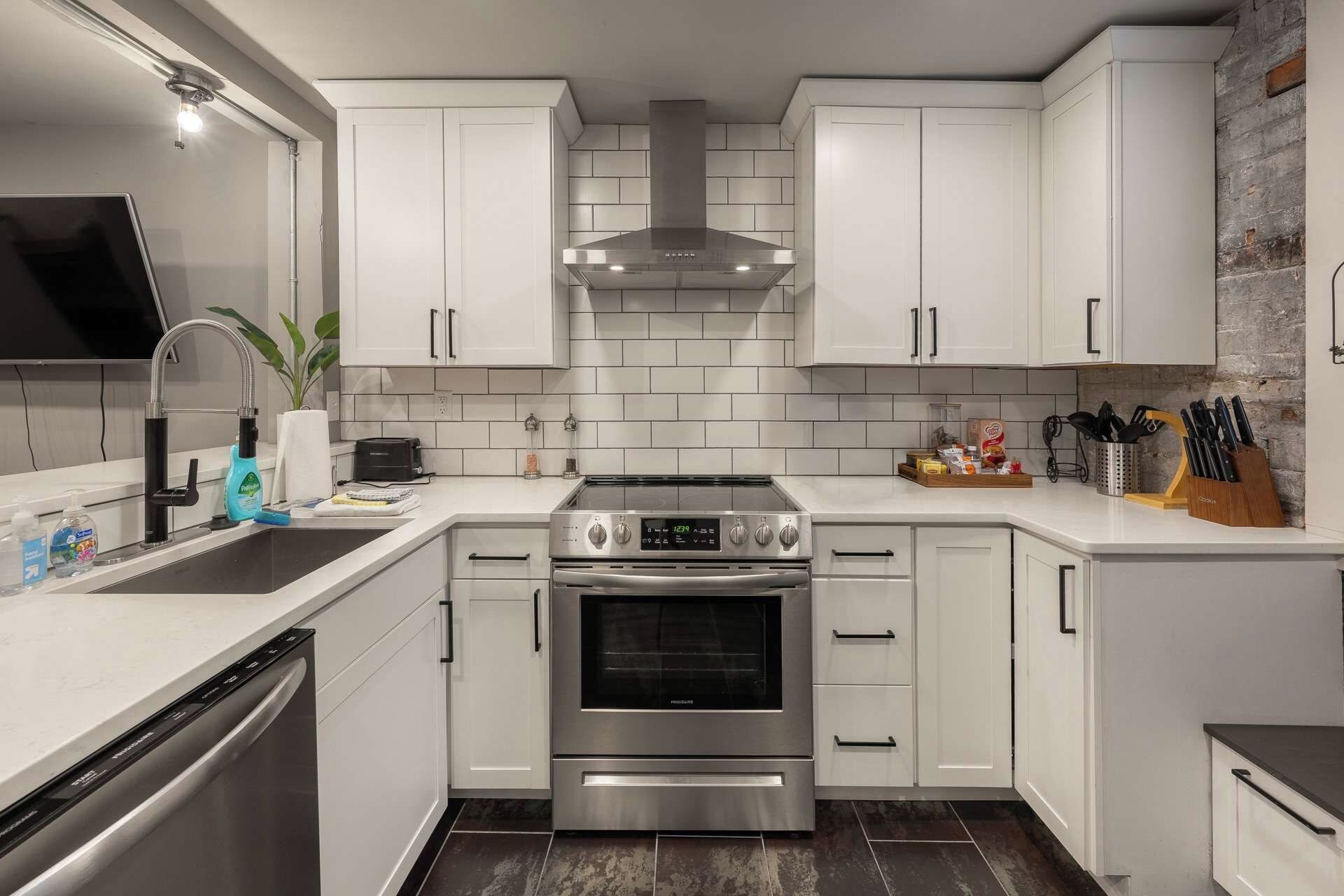 A modern kitchen with white cabinetry, stainless steel appliances, and a brick accent wall.