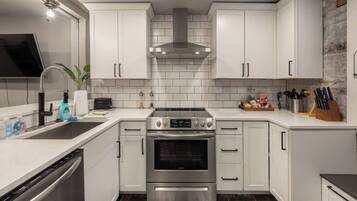 A modern kitchen with white cabinetry, stainless steel appliances, and a brick accent wall.