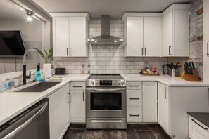 A modern kitchen with white cabinetry, stainless steel appliances, and a brick accent wall.