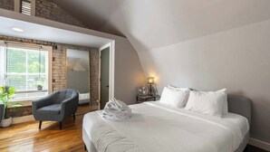 Un dormitorio con cama, una silla, una mesita de noche con lámpara y una ventana con persianas.