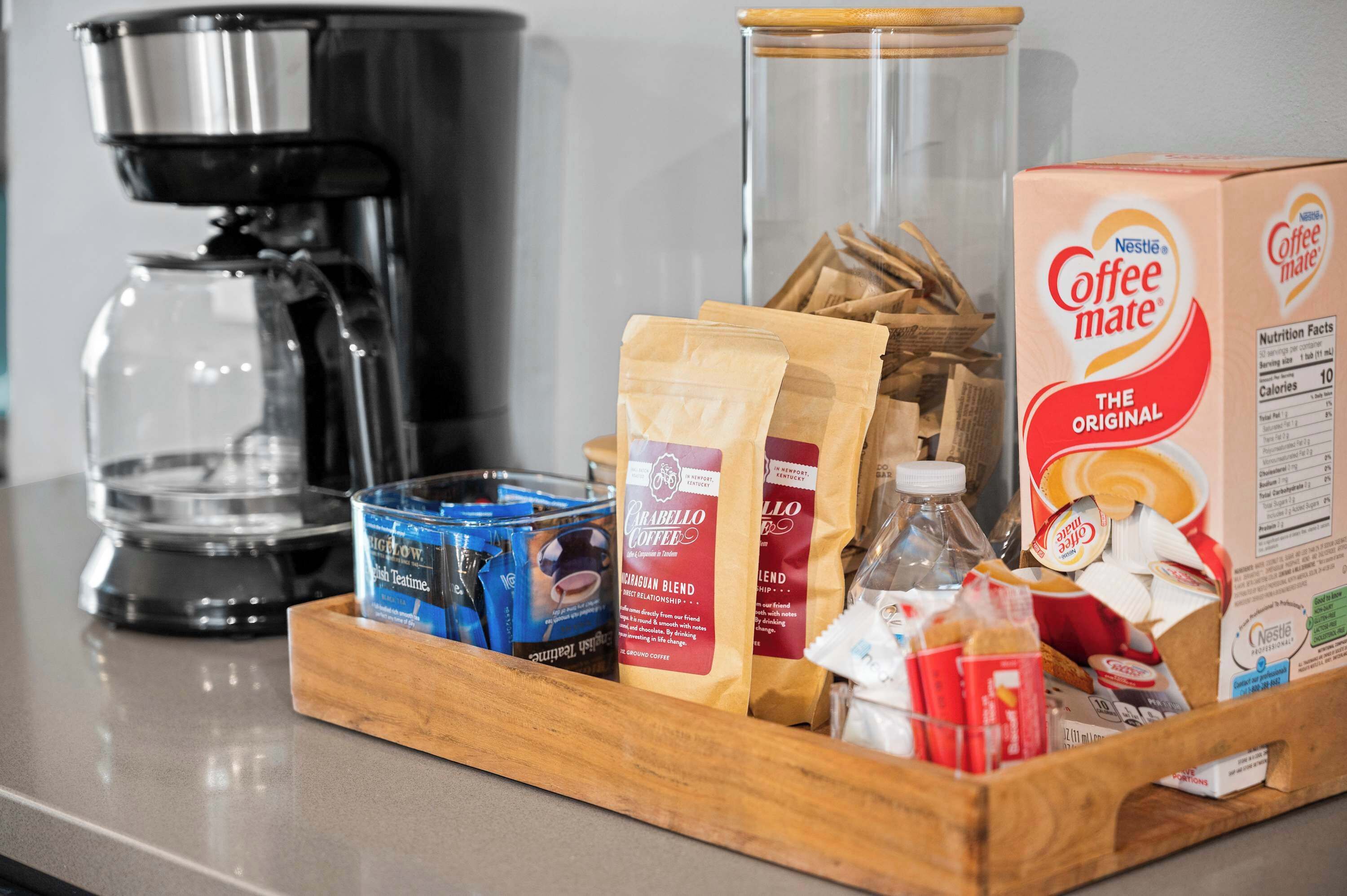 Un comptoir de cuisine avec une machine à café, des dosettes de café, un bocal en verre et des sachets de café.