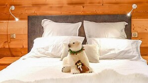 Un lit avec une literie et des oreillers blancs, une figurine d’ours polaire et une tête de lit en bois.