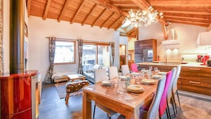 Un vaste espace de vie agrémenté d’un plafond en bois, d’une table à manger pour quatre personnes et d’un coin salon confortable.