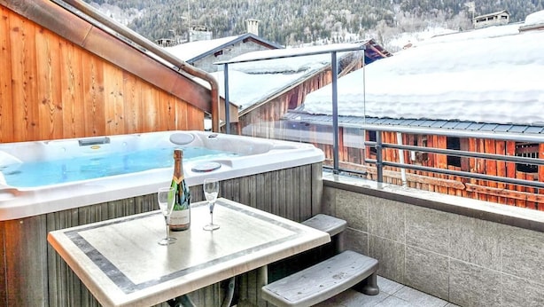 Un bain à remous avec une terrasse en bois et une table sur laquelle se trouvent une bouteille et un verre.
