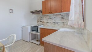 A compact kitchen with wooden cabinets, a marble backsplash, a built-in microwave, and a small refrigerator. - Villa Zina Studio 1 (Zagora-Mouresi)