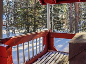 A wooden deck with a red railing overlooking a snowy forest.